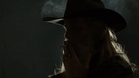 Closeup dark portrait: Backlit cowboy with long beard smokes cigarette - Powered by Shutterstock - Get 15% off with code: PIKWIZARD15
