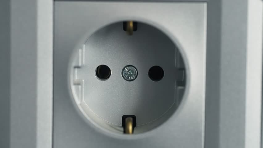 Close-up of a female hand inserting the plug of an electrical appliance into a socket.