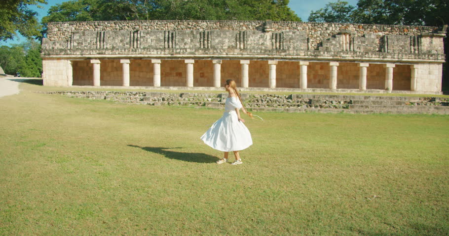 Woman twirling on grassy plaza in front of colonnaded ancient structure Mayan ruins