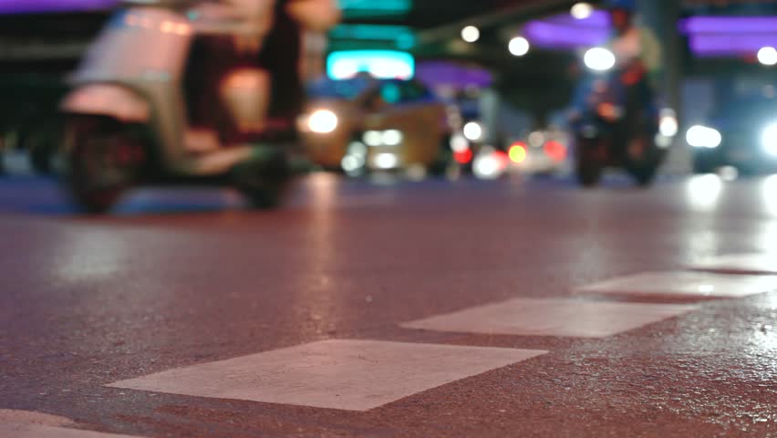 Close up of road surface marking on asphalt in Bangkok city at night rush hour. Blurred moving motorcycles and cars with bokeh lights in the background. Cinematic urban traffic scene