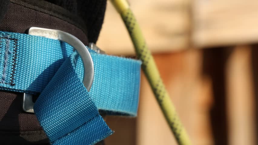 Close-up shot: hand securely clips a metal carabiner onto a D-ring of a yellow and black safety harness. Essential for climbing, adventure, and fall protection.