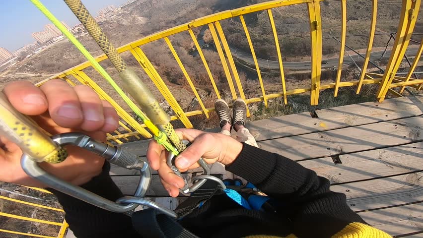 Man on exhilarating zipline speeds over urban canyon. Bridge with traffic and hazy cityscape in background. Thrilling extreme adventure sport, high-angle view.