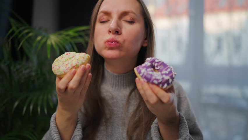 Woman with eating disorder eating two donuts with pleasure and at the same time