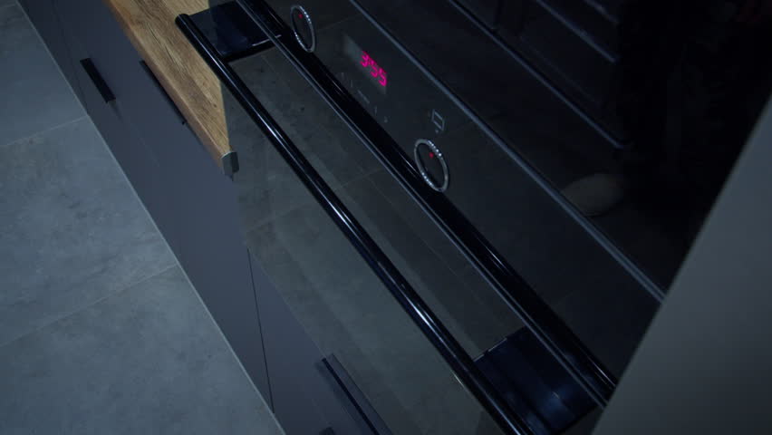 A man turns on the oven and puts on a homemade pizza to cook