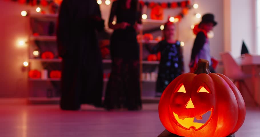 Happy mother, father and children having fun and dancing in living room in masquerade costumes celebrating Halloween party at home with pumpkin in foreground. Family celebration concept. 4k video.