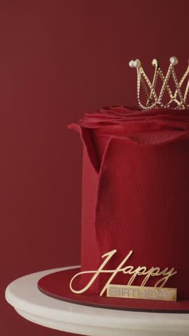 Beautiful queen or princess themed red cake with mastic rose petals in the shape of flower. Luxury rose shaped birthday cake with red velvet coating decorated with golden crown. Red background.