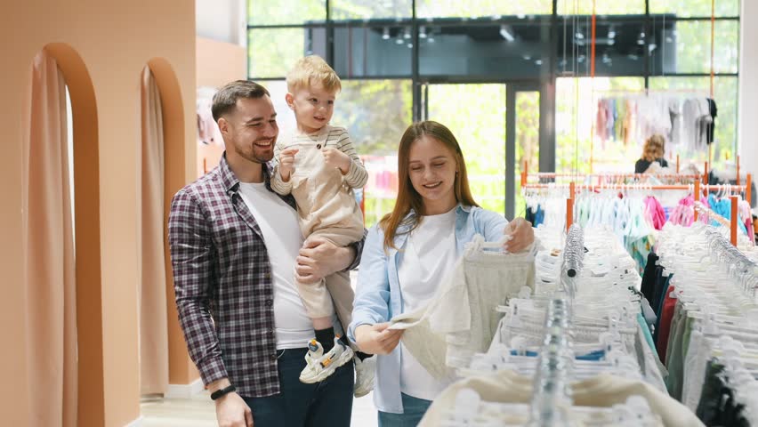 Holding boy in hands. Father, son and pregnant mother are in kid's clothing store.