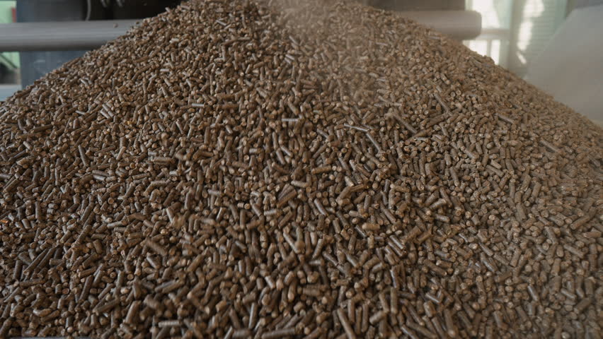 Close-up view in slow motion of brown cylindrical pellets being unloaded onto a metal grate in a large-scale industrial food production facility