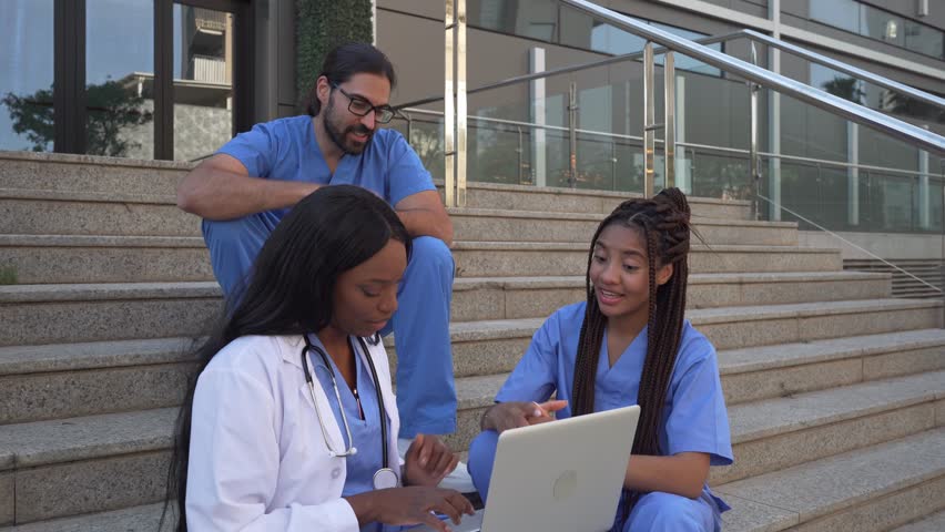 Video of Medical team discussing patient data on laptop sitting on steps outdoors