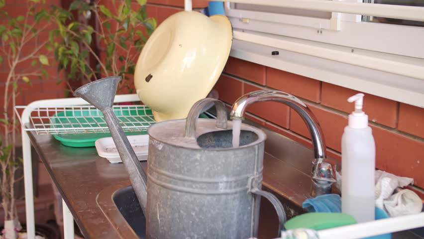 Watering can being filled at outdoor garden kitchen sink
