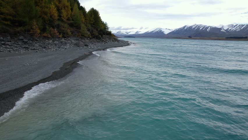 Waves In The Coastline Of Lake Tekapo With Snowy Mountains In The Background In South Island, New Zealand. - aerial shot