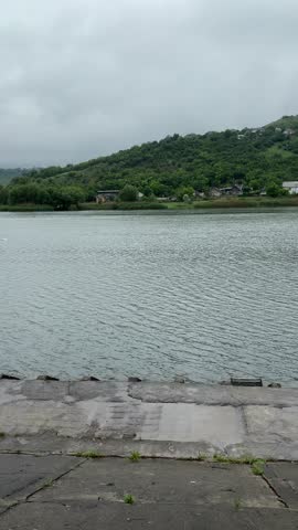 A park after rain on a cloudy day. A wet red brick path winds through lush green trees and grass. Benches and a gazebo are visible in the background.