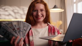 Portrait smiling happy Caucasian woman looking at camera celebrate holding money cash prize bet winning reward with laptop computer girl female user gamer gambler achieve with dollars casino at home - Powered by Shutterstock - Get 15% off with code: PIKWIZARD15
