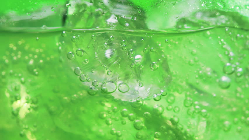 Close-up, refreshing sparkling drinking water being poured into glass with ice on green background. Bubbles in a glass. Minerals and Health Concept. 4K Slow Motion Video
