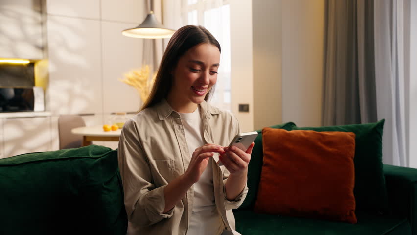 Caucasian woman girl female lady using mobile phone apps modern technology website at couch at home in living room relaxation browsing smartphone application social media order food delivery online