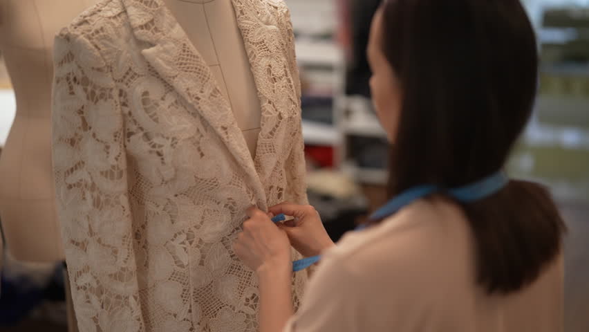 Back view of fashion designer taking measurements of white lace blazer draped on mannequin, ensuring perfect fit and crafting high-quality garment in atelier. Concept of garment manufacturing.