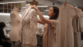 Dressmaker taking measurements of white lace jacket on mannequin, working in sewing workshop with other tailors and various clothes and supplies. Concept of sewing manufacturing, slow motion. - Powered by Shutterstock - Get 15% off with code: PIKWIZARD15