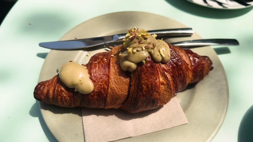 Freshly baked croissant with pistachio filling on a table on a sunny day in a restaurant. High quality 4k footage
