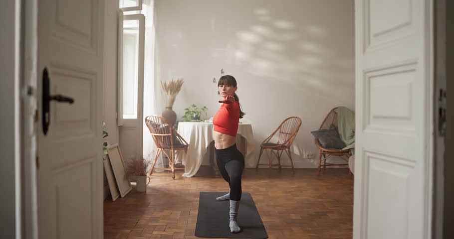 Girl in sportswear starts her yoga and meditation and gets into warrior pose on gym mat at home. Beginning of yoga and gassho position at home