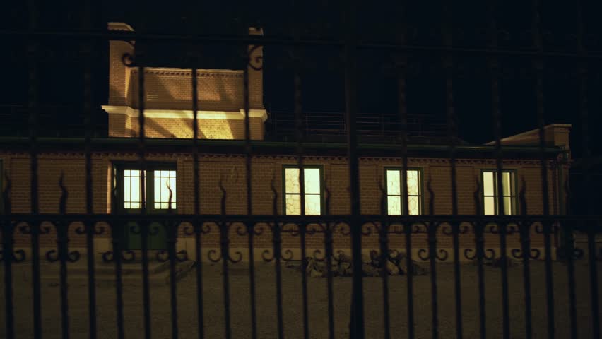 Nighttime view of a building with illuminated windows, seen through a wrought iron gate, creating a sense of mystery in Zagreb, Croatia
