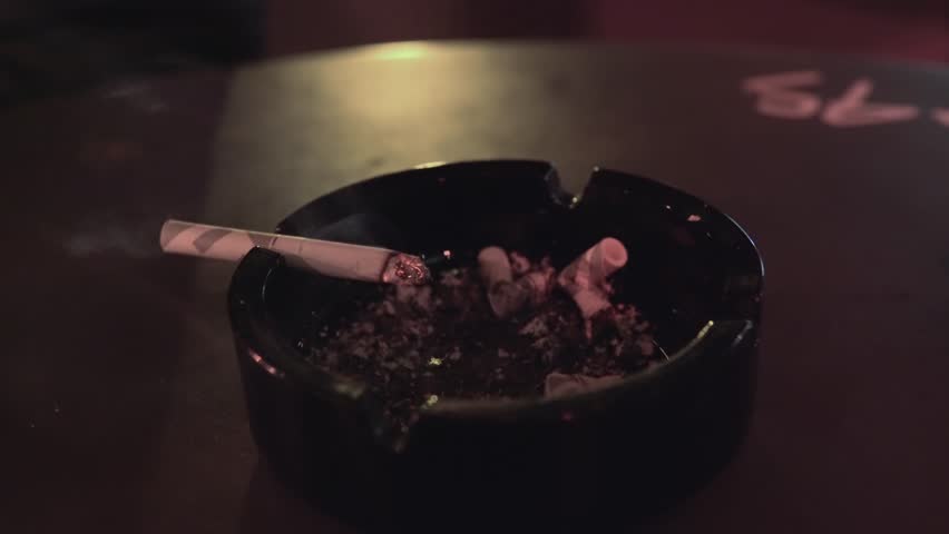 Lit burning cigarette resting in an ashtray on a dimly lit table in restaurant or caffee