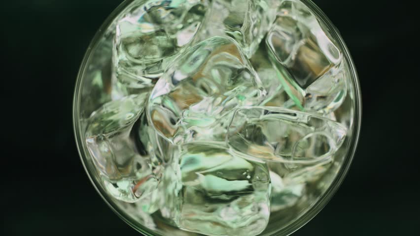 Super slow motion 1000fps top view on pouring beer on green ice cubes in rotate glass.Poured glass beer.Slow motion pouring beer on spin ice cubes in twist cup drink.Slow motion rotate turn ice cubes