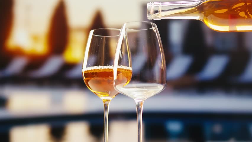 Orange or white rose wine bottle and glass against a sunset in a peaceful vineyard, pouring of ecological natural wine in hotel or sunset bar restaurant, cheers friends.