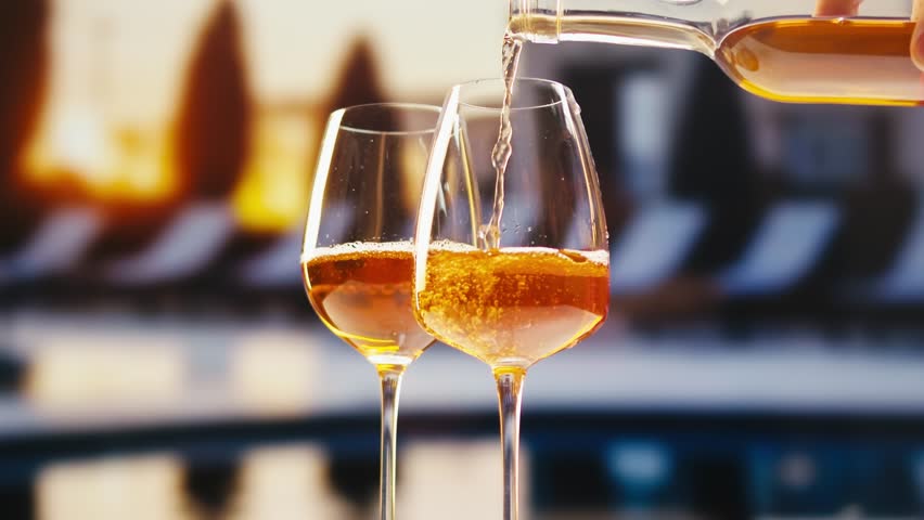 Orange or white rose wine bottle and glass against a sunset in a peaceful vineyard, pouring of ecological natural wine in hotel or sunset bar restaurant, cheers friends.