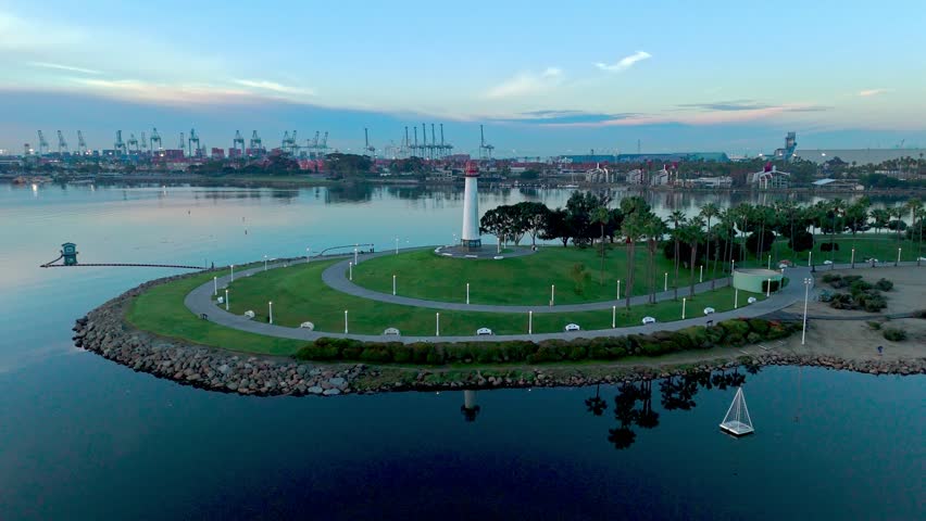 Aerial orbit shot of Lions Lighthouse and Shoreline Aquatic Park at sunrise, revealing calm waters with reflections of the sky, Long Beach, California.