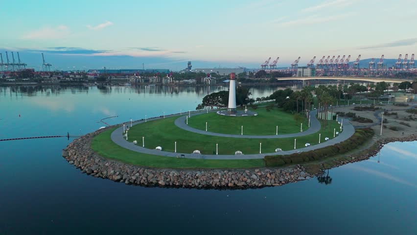 Aerial orbit shot of Lions Lighthouse and Shoreline Aquatic Park at sunrise, revealing calm waters with reflections of the sky, Long Beach, California.