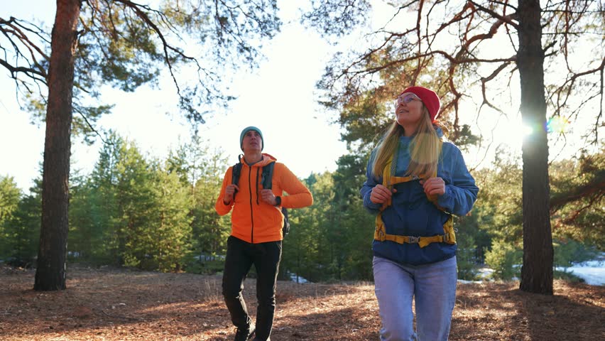 Two people travel through forest on sunny day. Exploring nature and enjoying outdoor lifestyle. Adventurous lifestyle in forest setting. Travel and hiking through wooded area. People embrace outdoor