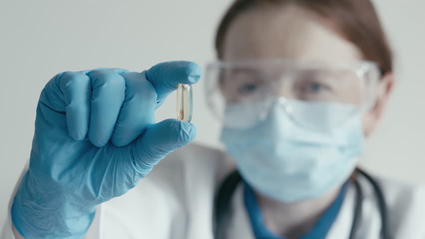 A researcher in protective gear inspects a pharmaceutical capsule, emphasizing the precision and commitment vital in pharmaceutical research to enhance healthcare and patient outcomes