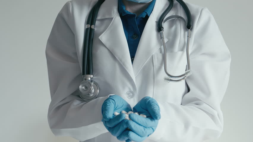 A healthcare professional in a white coat and blue gloves presents various white capsules, highlighting the crucial role of pharmaceuticals in effective medical treatment and patient care