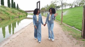 Two happy twin sisters wearing denim jackets and jeans, holding hands and walking along a canal in a green park - Powered by Shutterstock - Get 15% off with code: PIKWIZARD15
