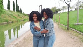 Two happy twin sisters wearing denim jackets and jeans, holding hands and walking near a canal in a city park - Powered by Shutterstock - Get 15% off with code: PIKWIZARD15