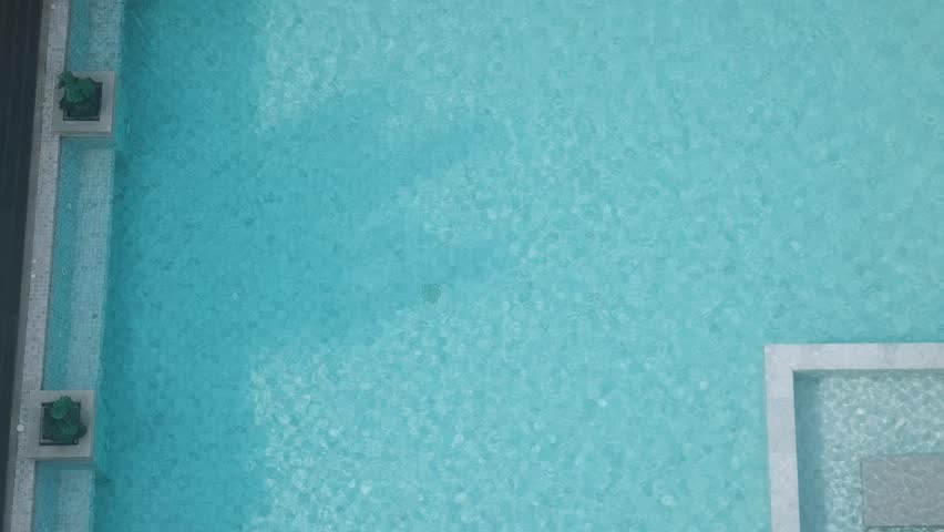 Top view of clean swimming pool in tropical resort with light blue water, textured tiles and subtle ripples, Phuket island, Thailand. Summer relaxation, luxury lifestyle, hotel vacation