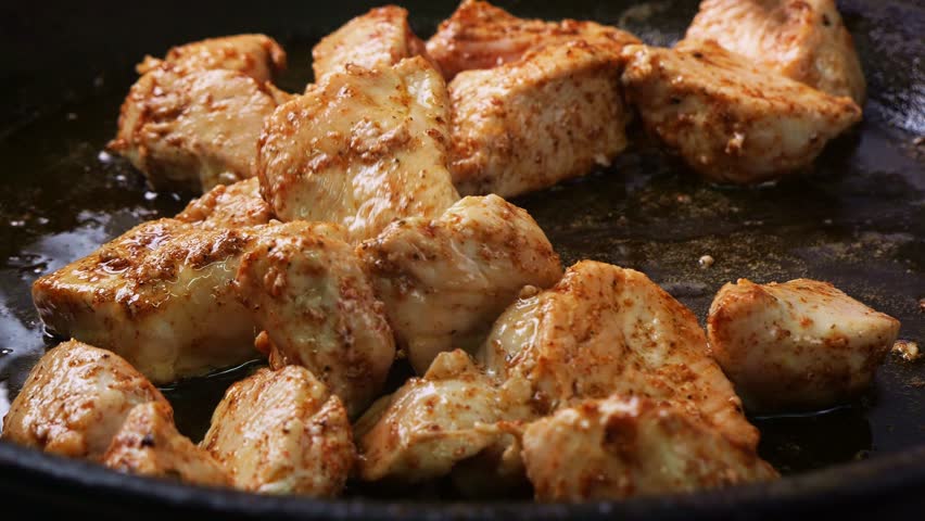 Chicken breast pieces are fried in spices and teriyaki sauce in oil in a frying pan. Medium shot.