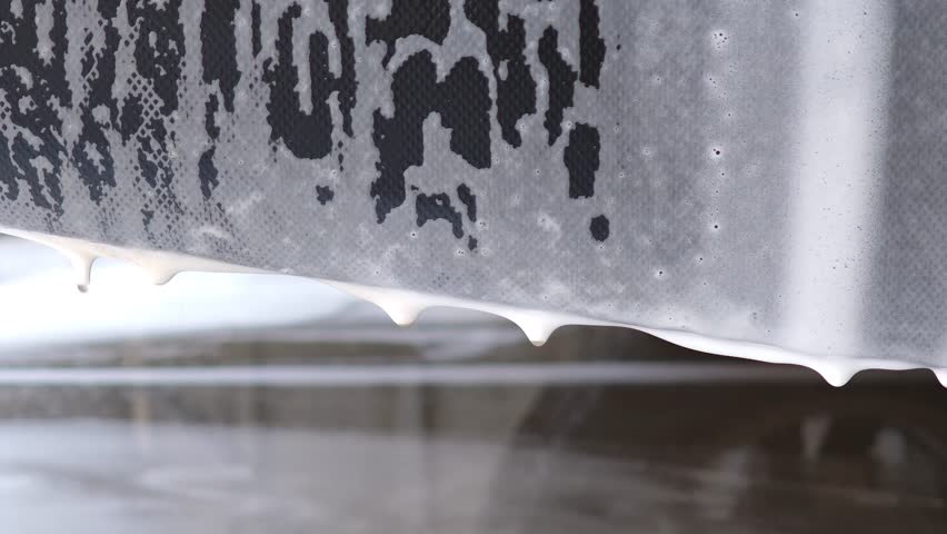 White soap suds dripping from a black car wash brush