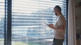 Mature man adjusting windows blind in the kitchen by tablet. - Powered by Shutterstock - Get 15% off with code: PIKWIZARD15