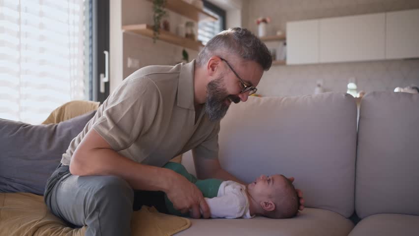 Father playing with his baby boy on sofa.