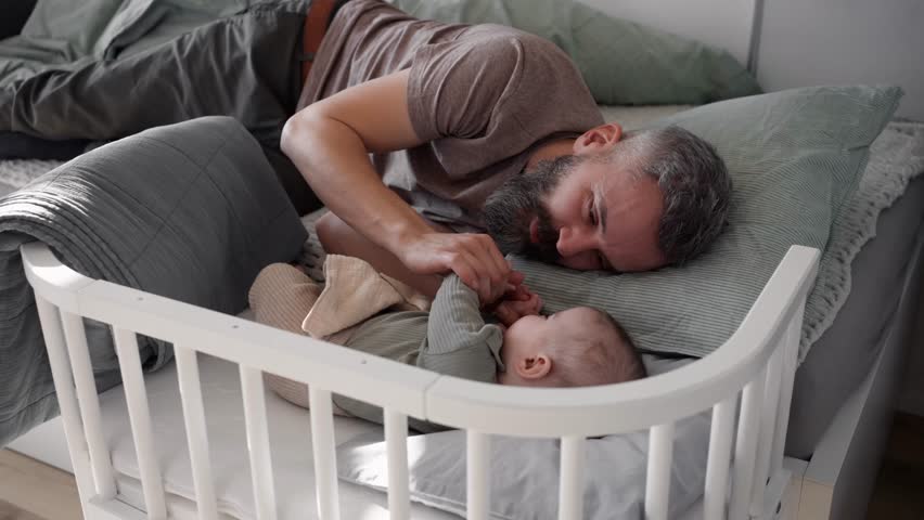 Father putting the baby to sleep, lying next to him in the crib.
