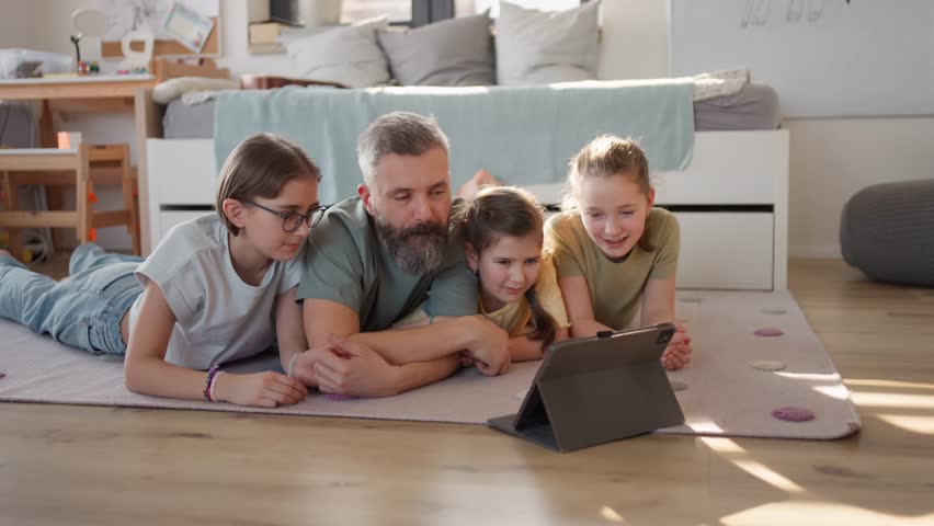 Video of father with three daughters watching tv show on tablet.