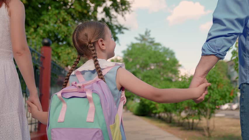 Girl child with parents go to school. Concept of children education. Child daughter with backpacks, father mother go to school holding hands. Happy family. Mother father take child to school on street
