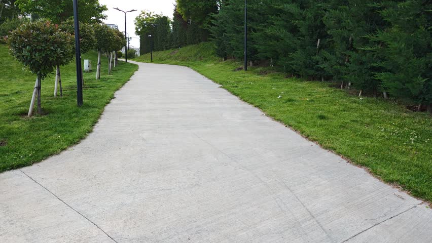 Smooth concrete path meanders through lush green park, offering serene escape in residential neighborhood