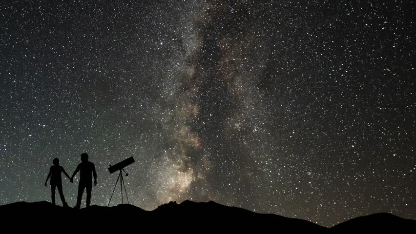 The lovers with telescope  stands on the hill on the  Milky Way galaxy and  mountains background. Night tight landscape starry sky.