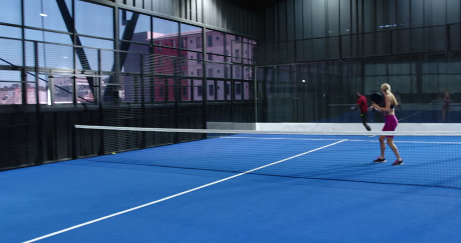 Young adults playing padel tennis on blue indoor court, enjoying competitive match. Sports, racket, teamwork, competition, recreation, athletic