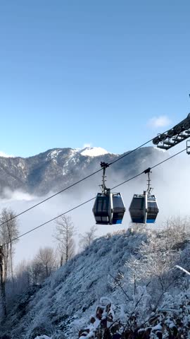 Cable cars glide above a frosty forest with snow-covered mountains and clouds. Gabala, Azerbaijan