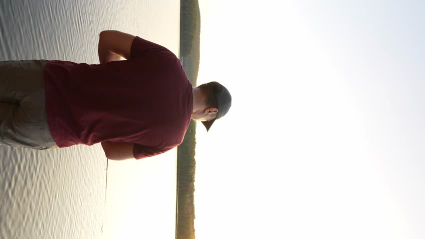 Man Fishing on the lake, Pulls a Reel of Fishing Line at Sunset in Summer, Close-up. Fisherman Catches a Fish. Fisherman With Spinning Rod in His Hand.