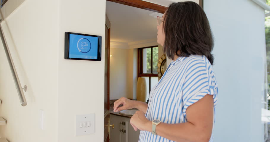 Senior diverse couple adjusting smart thermostat at home, smiling and discussing settings. Technology, home automation, elderly diverse couple, smart home, digital device, comfort