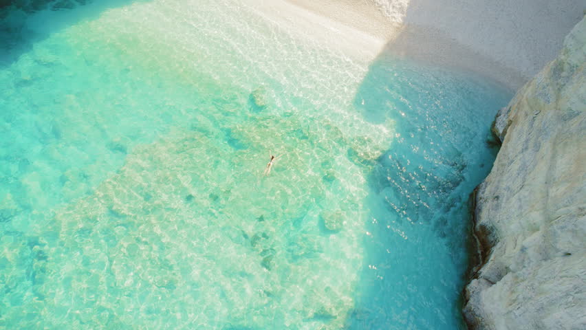 Person swims in transparent turquoise water near secluded cave beach in Kefalonia